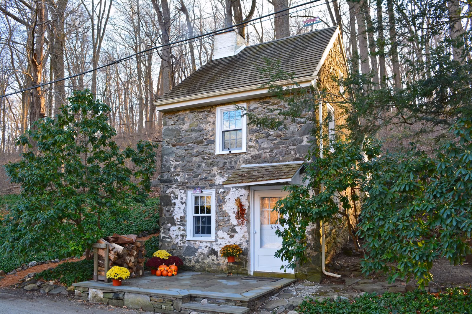 A small stone mill workers' cottage with a white door, decorated for fall, in Ridley Creek State Park